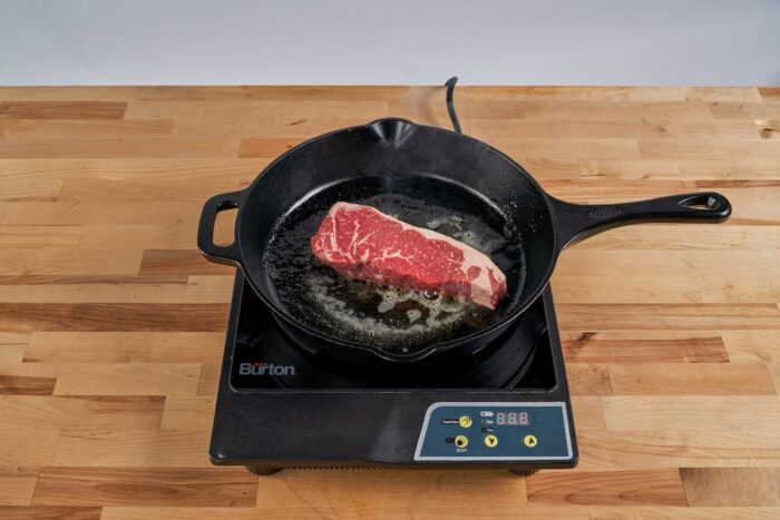 new york strip steak pan frying in cast iron